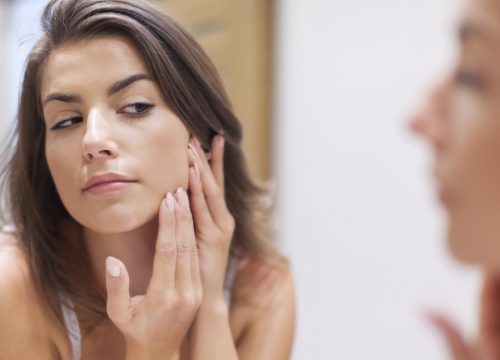 Woman checking her face in the mirror for acne and acne scarring